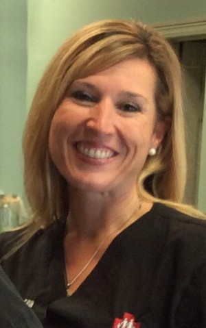 A woman wearing nurse's scrubs smiles at the camera